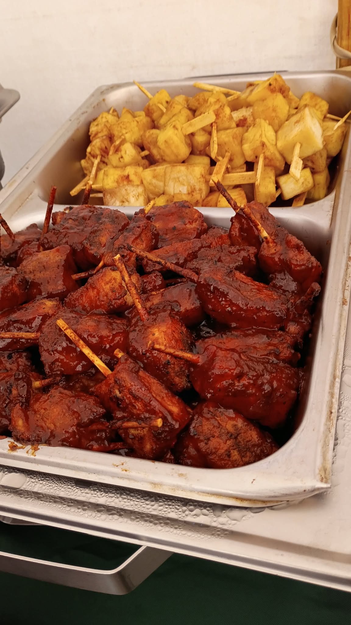 Skewered barbecue-glazed meat bites in a chafing dish next to skewered grilled pineapple chunks