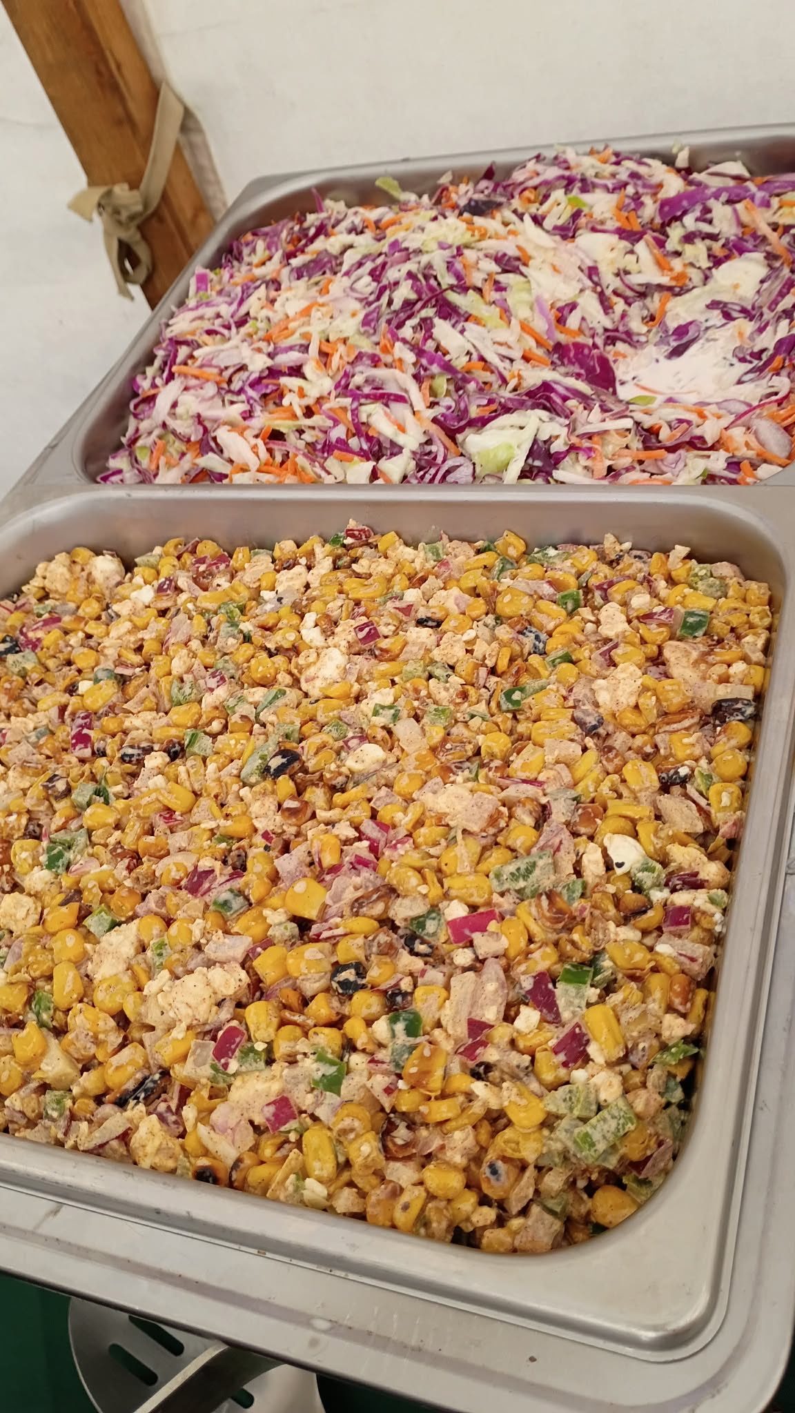 A pan of purple and green coleslaw above a pan of street corn salad with feta, peppers, and red onion